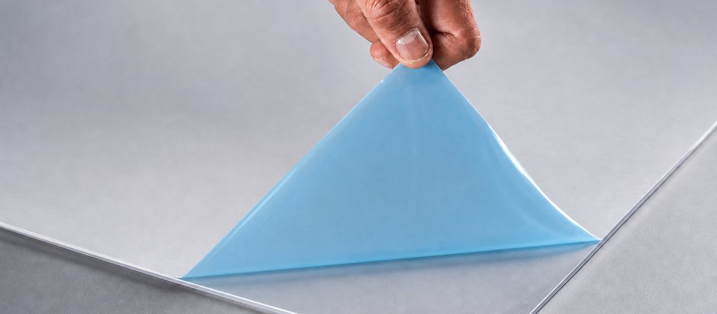 Una mano retirando por una esquina la película protectora azul de una lámina de acrílico transparente